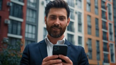 Beyaz, yakışıklı, profesyonel iş adamı orta yaşlı bir adam şehir dışında cep telefonu işi yapıyor cep telefonuyla sohbet ediyor SMS okuyor e-bankacılık uygulaması ekommerce modern teknoloji kavramını kullanıyor