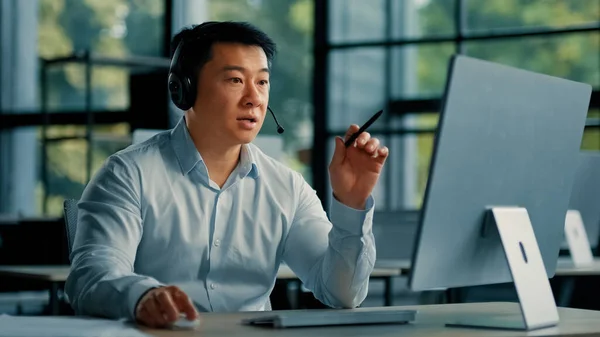 Chinese male asian mature businessman consultant office manager korean man in headphones communicate online use computer video call application take part in virtual briefing explain business strategy