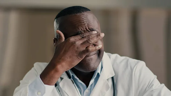 Tired african man doctor physician practitioner medical worker rub irritated eyes massaging face male ethnic therapist exhausted after working day feel chronic fatigue disease symptom health problem