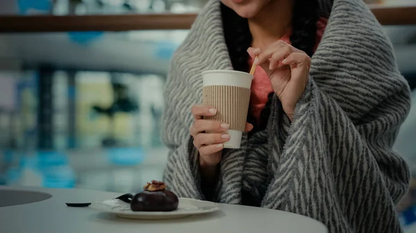 Unknown visitor woman client shopper girl rest at cafe restaurant cafeteria after shopping day wears blanket drinking aroma hot coffee tea from cup ordering chocolate cake enjoy delicious sweet desert
