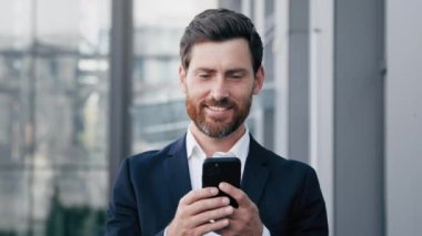 Kapalı kapılar ardında gülümseyen adam elinde cep telefonuyla akıllı telefon ekranına bakıyor memnun iş adamı müşterisi e-posta yoluyla iyi haberler alıyor ve sosyal ağda mesaj yazıyor.