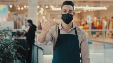 Dost canlısı etnik garson, kafeterya lokantası müdürü, tıbbi maskeli küçük işletme sahibi, önlüklü hoş geldin pazarlamacısı, davetkar müşterileri davet ediyor.