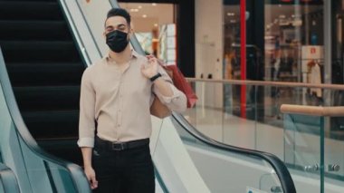 Hint modasına uygun etnik iş adamı, modaya uyan erkek tüketici tüketici müşterisi, yüzü morarmış tıbbi maske takan, merdivenlerin yanındaki mağazadan alışveriş torbaları alan,