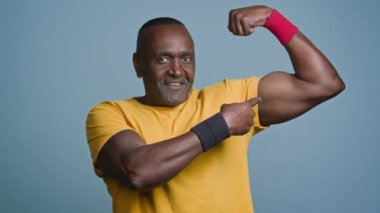 Gülümseyen olgun erkek sporcu gri arka planda duruyor. Büyük erkeksi kaslarını gösteriyor. Pompalı pazılar, erkek spor eğitmeni fitness eğitmeni trisepslerin spor yapmaya motive olduğunu gösteriyor.