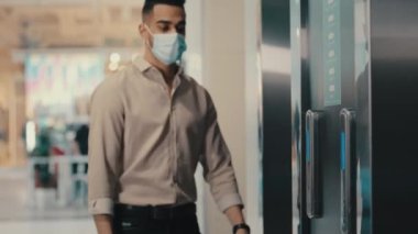 Endişeli Hintli Latin kökenli işadamı tıbbi maske takan patron şirket ofisindeki girişimci asansör düğmesine basarak kol saatine bakıyor.