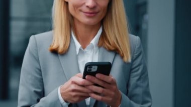 Yakın plan gülümseyen iş kadını elinde cep telefonu e-postası tutuyor sosyal ağlara mesaj gönderiyor dışarıda duran mutlu kadın müşteri akıllı telefon hareketleriyle online mağazadan alışveriş yapıyor.