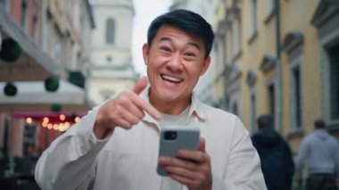 Mutlu gülümseyen heyecanlı adam elinde cep telefonuyla iyi haberler okuyor e-posta alıyor memnun erkek müşteri akıllı telefon ekranını işaret ediyor e-bankacılık online hizmetinden memnun.
