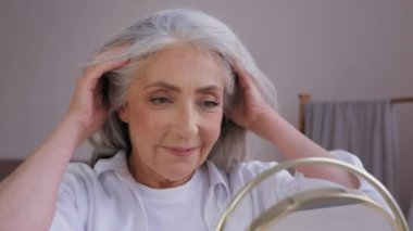 Aynadaki yansımaya bakan yaşlı yaşlı olgun kadın modelini kapatın. Doğal keratin şampuanı temizleme işlemi sonucu 60 yaşında beyaz bir kadının uzun saç bakımına dokunması sonucu ortaya çıktı.