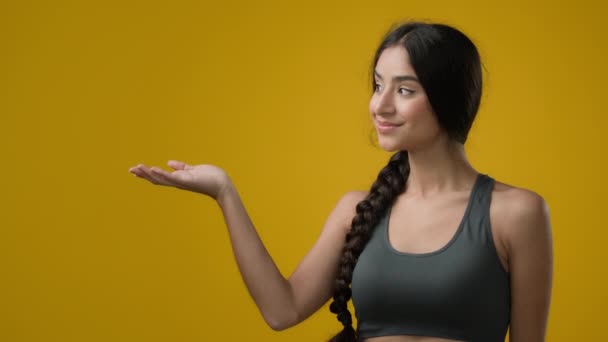 ポートレートスタジオでインドの20代の女性黄色の背景は脇に手のひらアームポイント広告で側面を指しています プロモーションは 空のスコープスペースに示す奨励賞の看板の女の子の女性をお勧めします — ストック動画