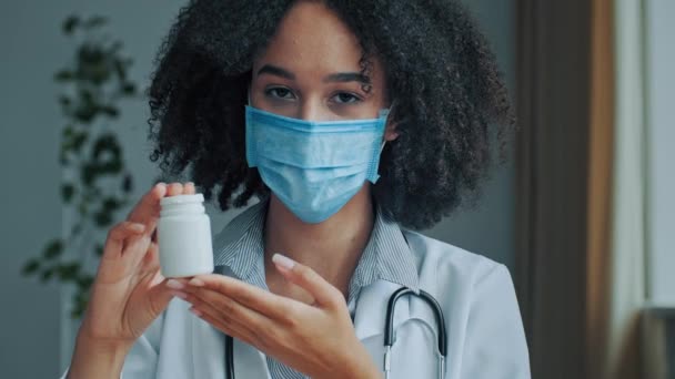 戴口罩的非洲女医生心脏病专家顾问在摄像机前展示了药丸广告维生素药物抗生素药物在药店的有效治疗销售 — 图库视频影像