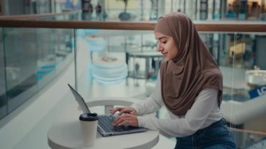 Arap müslüman kız işkadını alışveriş merkezinde dizüstü bilgisayar üzerinde çalışıyor. İnternette iletişim kuruyor, uzaktan arama işi yapıyor. Çevrimiçi Ortadoğu İslamcı kadın alışverişi yapıyor.