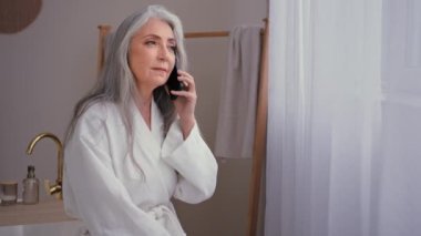 Kafkasyalı 60 'lı yaşlarda, yaşlı bir kadın banyoda konuşan olgun bir kadın. 50' li yaşlarda, yaşlı, akıllı telefon büyükannesi ile konuşan yaşlı bir kadın. Hücrenin otel banyosunda hidrat kozmetik ürünleri sipariş ettiğini söylüyor.