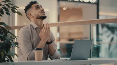 Hint asıllı etnik işadamı, kafede dizüstü bilgisayarlı bir erkek, şans için Tanrı 'ya dua ediyor, şans diliyor, kazanmak için dua ediyor, bahsi kutluyor, online piyango kazanıyor.