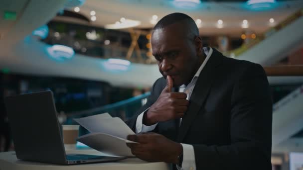 中年の大人の集中的な思考思慮深い男アフリカの起業家のビジネスマンは 書類作業員と作業紙をチェック書類作成プロジェクトを検査ノートパソコンの会計で仕事を考える — ストック動画