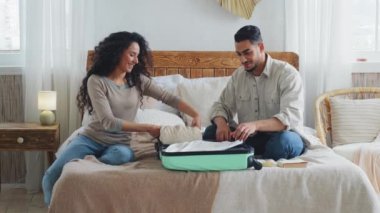 İspanyol Hintli Arap çift evli eşler karı koca sevgili kadın ve sakallı adam yatak odasında oturuyor eşyalarınızı bavula koyup seyahat balayına gidiyor.