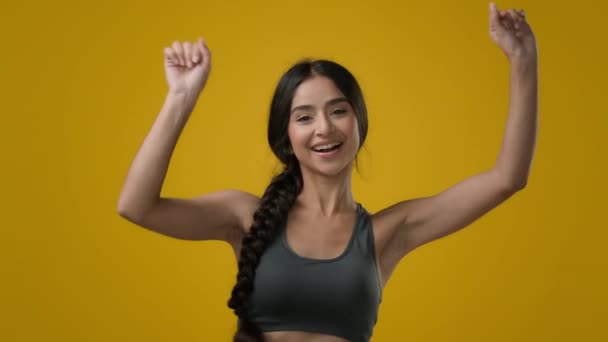 演播室里的女性黄背景印度20多岁的女运动员穿着运动服的女运动员快乐地跳舞有趣地跳着舞走向音乐运动派对庆祝胜利 — 图库视频影像