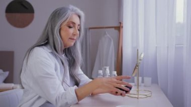 Beyaz saçlı, yaşlı, nemlendirici elleri ve doğal organik kremi olan yaşlı, yaşlı bir kadın büyükanne avuçlarını nemlendirmek için vücut losyonu sürüyor.