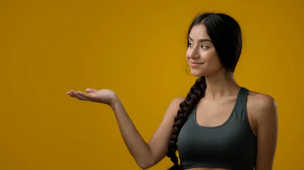 肖像画20多岁的印度女子在演播室黄色背景下指着旁边的手掌手尖广告 促销推荐奖签约女郎展示空旷的应对空间 — 图库照片