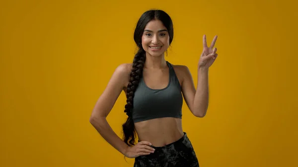 笑印度裔女体育女女运动员在黄色演播室背景中表现出双指手势两个2数字胜利手势和平手势手势显示V型手势臂两秒获胜 — 图库照片