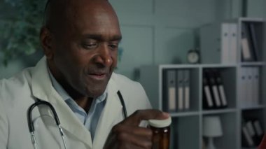 Afrikalı yetişkin doktor erkek doktor hasta kadın hastayla konuşuyor. İçinde vitamin hapları ve bağışıklık hapları olan ilaç talimatları veriyor. Genç Arap kadın klinikte ilaç yardımı alıyor.
