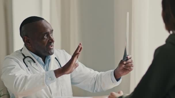 アフリカ系アメリカ人男性医師成熟した男性放射線医外科医はX線検査結果を見て 病院で放射線スキャンの患者チェックの健康状態とMri画像の話を探る — ストック動画