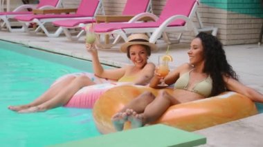 Mutlu, gülen beyaz kadınlar ve tatil tatillerini lüks bir havuz kaplıcasında buzlu kokteyller içerek geçiren Arap kadınlar. Şişirilebilir yaşam şamandıralarında yüzen iki güneşlenen kız arkadaş.