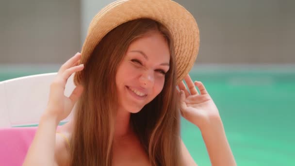 飘飘欲仙的高加索女人迷人的欧洲20多岁的姑娘千年模范游客头戴时髦的豪华草帽坐在游泳池边晒日光浴笑着享受夏日懒散的假期 — 图库视频影像