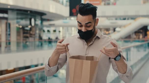 喜形于色的印度裔商人 戴着医用黑脸面具 30多岁的男人 买家客户 看看购物袋里面的购物袋 购物袋里装着什么东西 满意的样子 — 图库视频影像