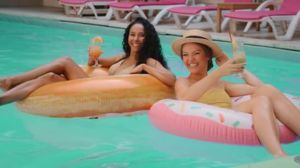 2人の美しい女性観光客の人々は 高級プールで水泳アルコールカクテルを飲む水着でスペイン語と白人の女の子の友人を日焼けさせました 夏の旅行の遊び心のある女性モデルは休日の週末を祝う — ストック動画