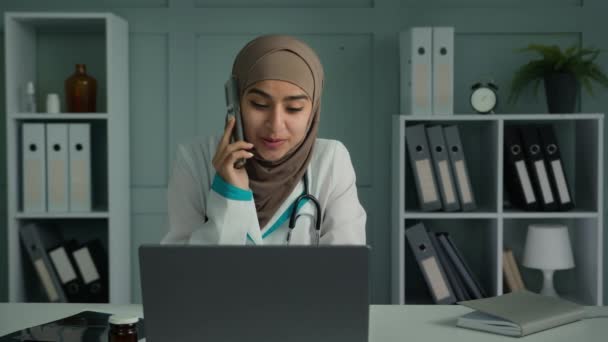 若いイスラム教徒の医師アラビア人女性医療専門看護師の話携帯電話仮想医療相談現代の技術スマートフォンを使用して遠隔医療援助を与える電話遠隔医療の概念に話す — ストック動画