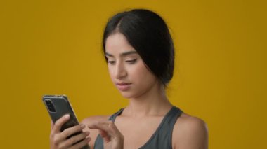 Hintli etnik kadın bayan gülümseme cep telefonuna göz gezdirirken cep telefonuna referans jesti ile bakarak cep telefonundan başparmağınızı kaldırarak online bahis kazandığınızı gösterin.