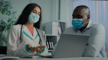 Yaşlı, hasta, Afrikalı bir erkek, tıbbi maskeli profesyonel kadın doktor, kadın pratisyen hekim, klinikte yetişkin hasta kontrolüne danışmanlık tavsiyesinde bulunuyor.