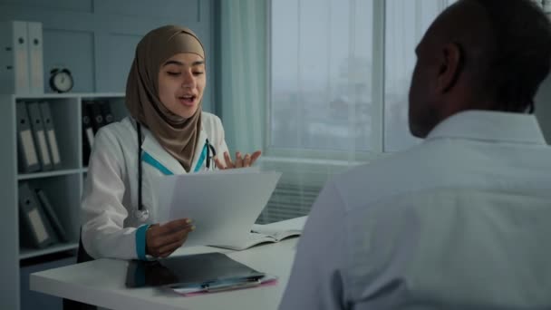 Opiekuńcza Młoda Kobieta Lekarz Prowadzący Wykazując Papierowe Badania Zdrowia Chorego — Wideo stockowe