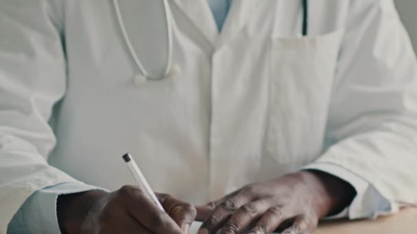 セラピストアフリカ系アメリカ人医師マスクの小児科医は 病院の診療所に座っている患者のための医学診断を書きます完全な医療保険健康診断私のレシピは 呼吸器を離陸 — ストック動画