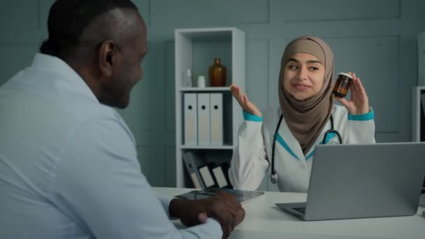 中東イスラム女性医師顧問薬剤師は不健康な老人を助ける若い薬瓶薬抗生物質丸薬心臓錠高齢者の病気の患者のための薬物リハビリテーションをお勧めします — ストック動画