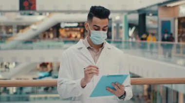 Etnik Hintli tıp çalışanı doktor kimyager yüz maskesi takan doktor kimyager ve laboratuvar önlüğü üniforması, sağlık güvenliğini içeride kontrol ediyor.