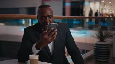 Kafede kahve içen Afrikalı Afrikalı Amerikalı işadamı iş adamı cep telefonu konferansı ile iş görüşmesi yapıyor. Orta yaşlı Afrikalı ciddi bir CEO omuz silkip sohbet ediyor.