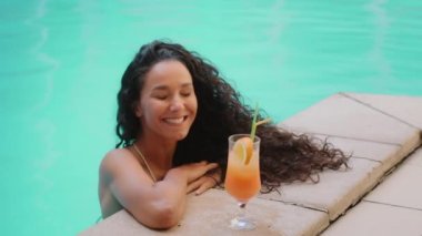 Latin Latin kıvırcık esmer kadın etnik Arap seksi kız arkadaş ferahlatıcı bir kokteyl kadın turist modeli içiyor yaz havuzunda yüzüyor tatilin tadını çıkarıyor iyi bir jest yap ve oteli onayla