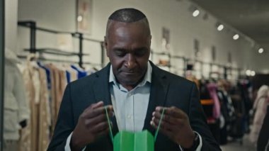 Orta yaşlı Afrikalı girişimci erkek portresi. Alışveriş çantasının içine bakıyor. Mutlu bir hediye paketi.