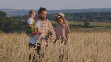 Kafkasyalı mutlu aile çiftçileri kızlarıyla birlikte sakallı adam ve sarışın kadın ve küçük kız çocuğu yaz günü buğday tarlasında yürüyorlar sonbahar hasadında yürüyüş haftasonunun keyfini çıkarıyorlar.