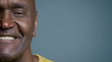 Kapalı yarı erkek yüzü, neşeli bir ifadeyle olgun Afrikalı Amerikalı bir adam kameraya bakıp gülümseyen sağlıklı beyaz dişli gülümseyen mutlu müşteri gri arka plan stüdyosunda poz vermekten memnun.