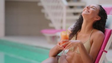 Güneş banyosu yapan, bronzlaşmış kadın turist, kıvırcık Arap, Latin, seksi kadın havuz kenarında dinlenen, havuz kenarında dinlenen, spa yapan, neşeli, flört eden yaz tatilinin tadını çıkarın.