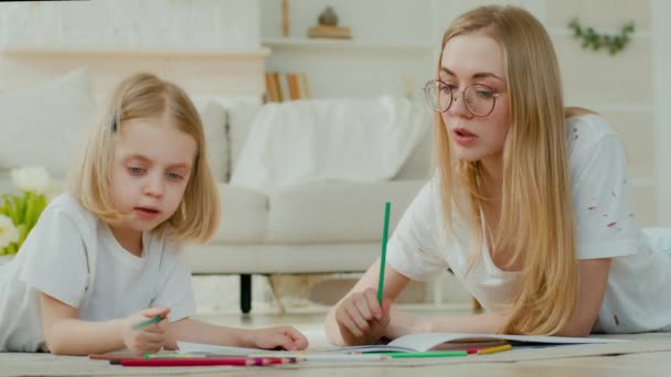 被收养的小女孩与白种人母亲一起欣赏绘画艺术 她们戴着眼镜躺在自家的地板上 和妈妈一起生女儿的小孩临时保姆老师用铅笔画图 — 图库视频影像