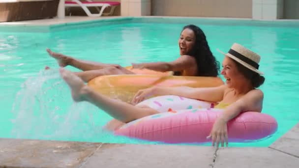 プールで泳いでいる2人の幸せな若いヒスパニック白人のガールフレンド千年紀の女性青い水は一緒に週末をお楽しみください休暇ボディレクリエーションと夏のエンターテイメント豪華なホテル予約 — ストック動画