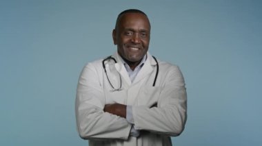 Gri arka plan stüdyosunda kollarını kavuşturmuş, kendinden emin mutlu bir doktor gülümseyen Afro-Amerikan erkek terapist doktor.