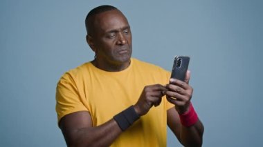 Yetişkin erkek atlet eğitmeni internet sportmeninden telefonda spor eğitimi videosu izliyor. Sosyal ağda güç egzersizi arıyor. Akıllı telefon ekranını işaret ediyor.