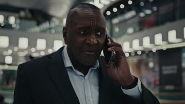 Yetişkin, orta yaşlı, yürüyen iş adamı Afrikalı ciddi, hayal kırıklığına uğramış, cep telefonu konuşan sinirli, kapalı alanda akıllı telefonla konuşan, çalışanın kötü pazarlığını vurgulayan, proje tartışması yapan bir adam.
