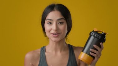 Web kamera görüntüsünü kapatın. Stüdyo sarı arka planda sporcu bayan sporcu bayan sporcu bayan talk show fitness şişesiyle su likörü protein kokteyli karıştırıcı ile konuşuyor.