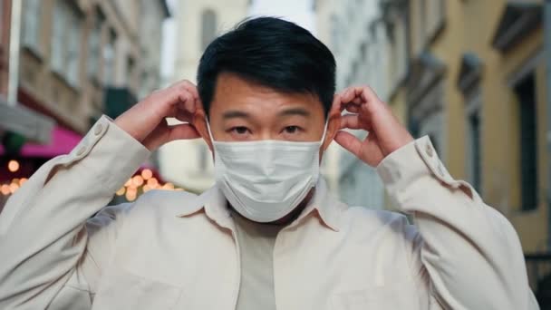 严重的亚洲男子头戴医用口罩 目光炯炯地看着站在室外的男性游客 戴着防护口罩 坚持检疫措施 防止传染病大流行 — 图库视频影像