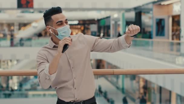 在公司的写字楼购物中心里 一位戴着医疗面罩的印度男性商人获奖者庆祝胜利 他用手机来庆祝胜利 并享受手机音频应用跳舞的乐趣 — 图库视频影像